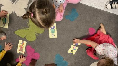 Dzieci siedzą na szarym dywanie w kolorowe motyle i układają obrazki
