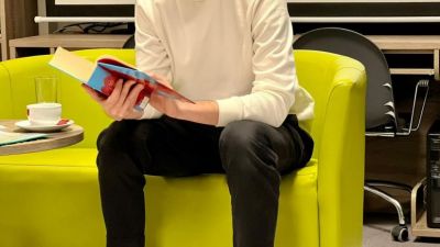 Filip Kosior siedzi na zielonej kanapie. Czyta fragment książki. W tle ekran na którym wyświetla się plakat promujący trwające już spotkanie autorskie