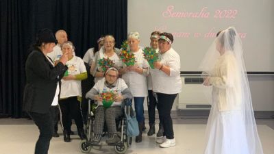 Grupa seniorów wystrojona w białe koszul, śpiewają i trzymają bukiety kwiatów